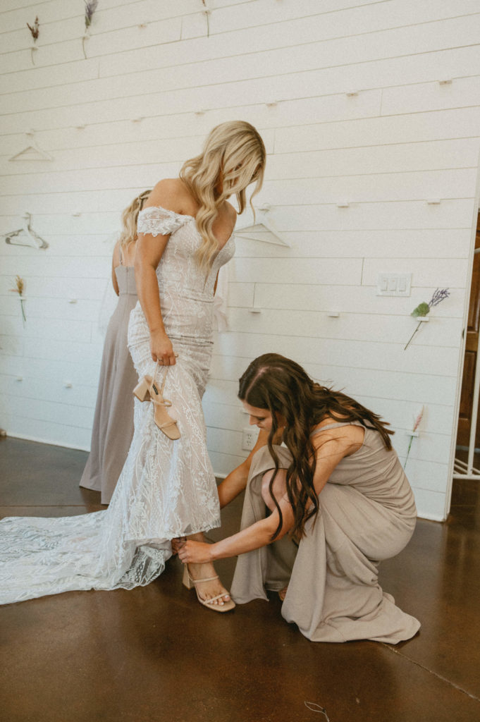 bridesmaid putting brides shoes on